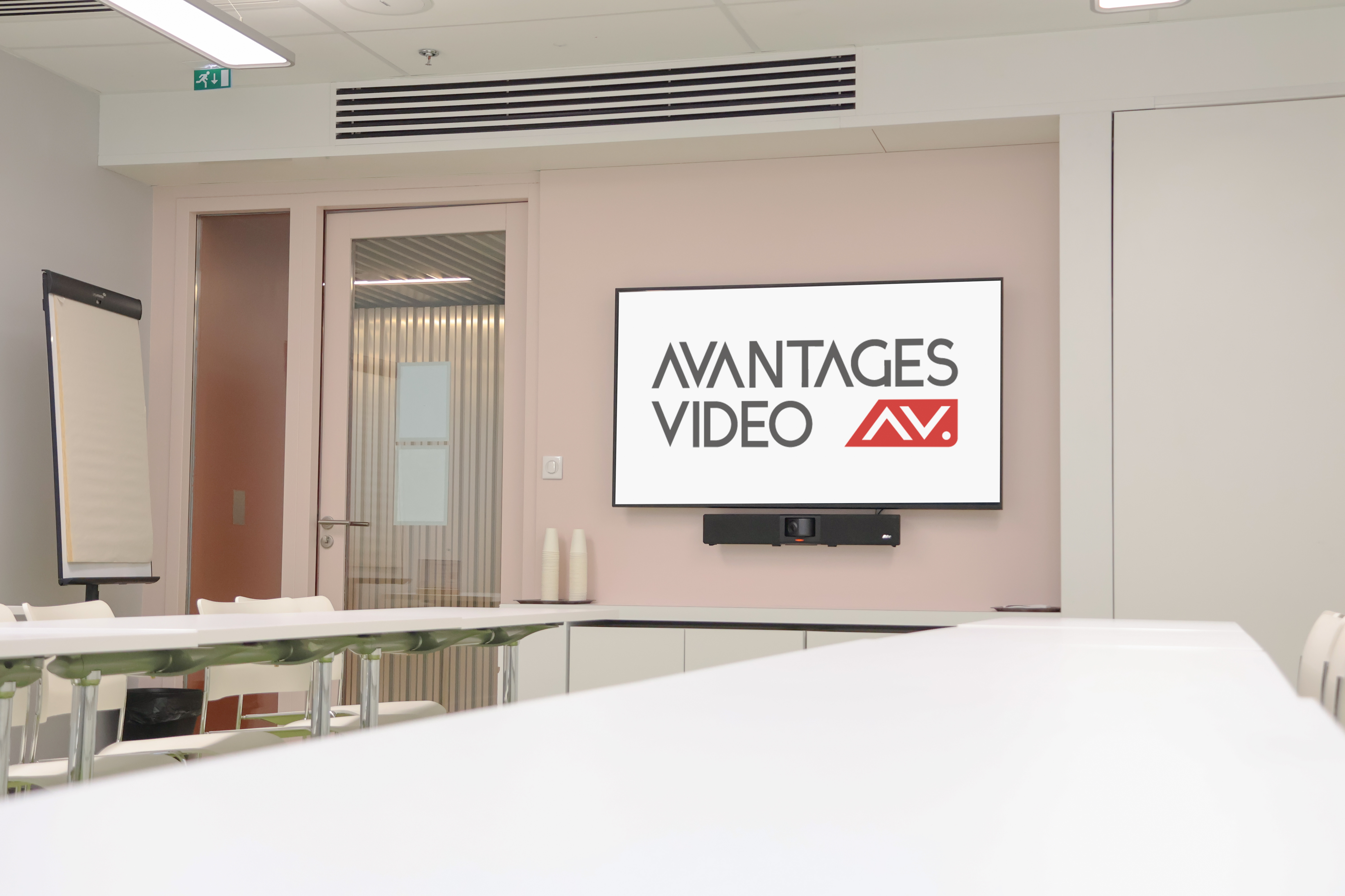 Salle de réunion moderne équipée d'un écran avec le logo Avantages Vidéo et d'une barre de visioconférence professionnelle fixée au mur.