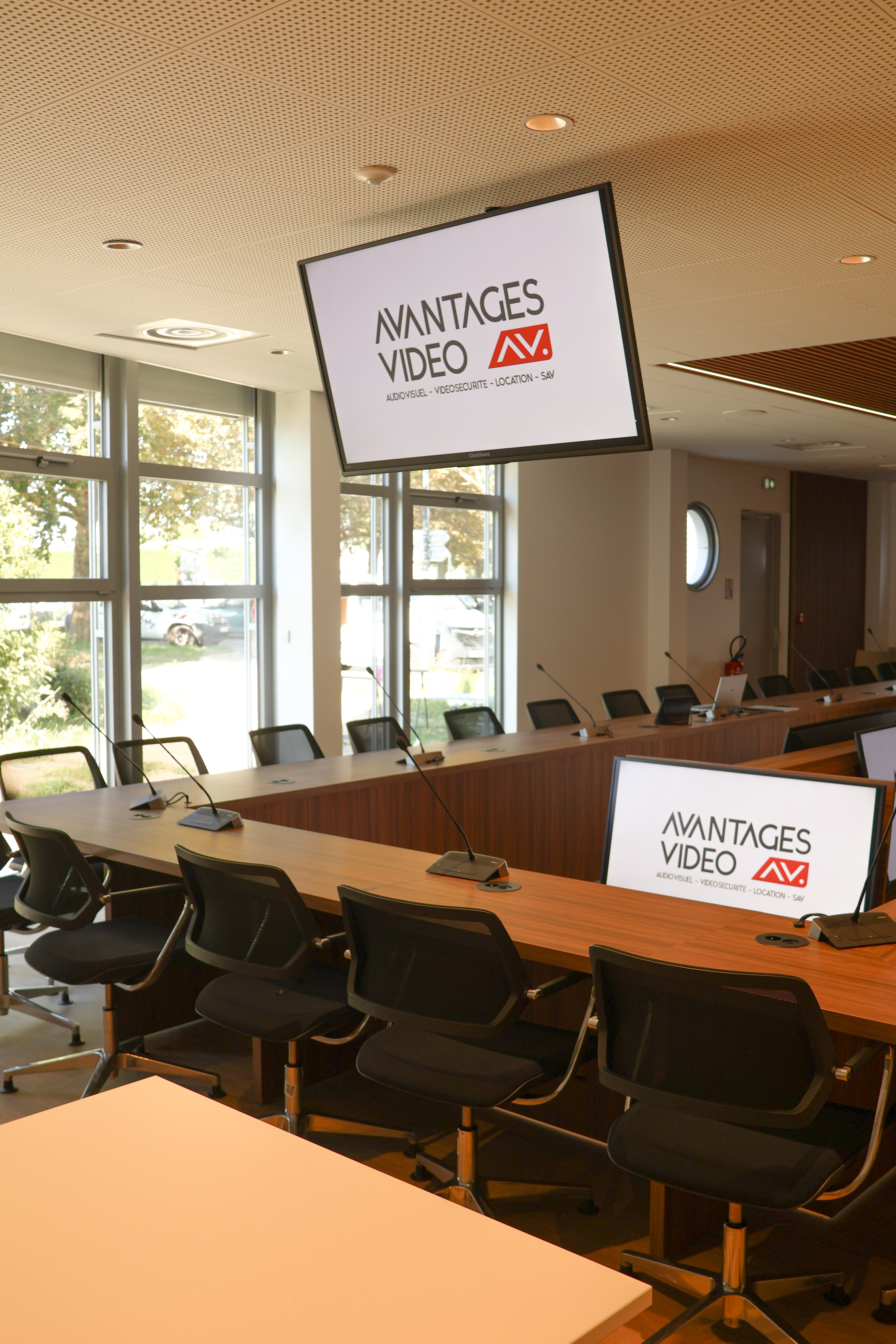 Salle de conseil équipée de micros, écrans de diffusion et mobilier professionnel, avec le logo Avantages Vidéo affiché à l’écran.